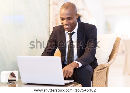 Business on the go. Cheerful young African businessman using his laptop while sitting at the restaurant