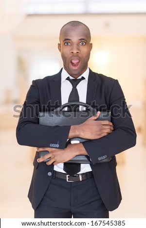 Frustrated businessman. Shocked young African man in full suit holding a bag in his hands and keeping mouth open while looking at camera