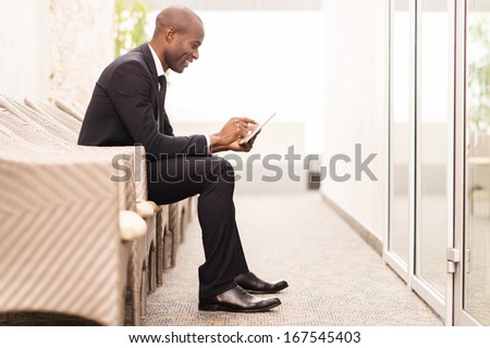 Checking his schedule on the go. Side view of cheerful young African businessman working on digital tablet while sitting on the chair