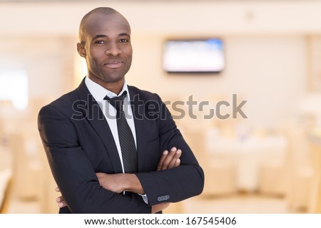 Confidence and charisma. Cheerful young African man in full suit keeping arms crossed and looking at camera