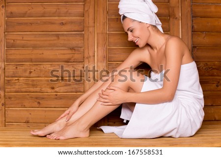 Woman in sauna. Attractive young woman wrapped in towel relaxing in sauna and smiling