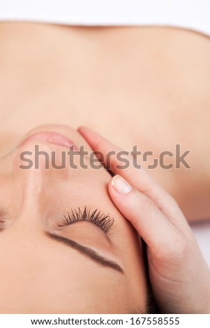 Facial massage. Top view of attractive young woman lying down and keeping eyes closed while massage therapist massaging her face