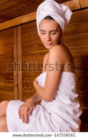 Beauty in sauna. Beautiful young woman wrapped in towel relaxing in sauna and keeping eyes closed