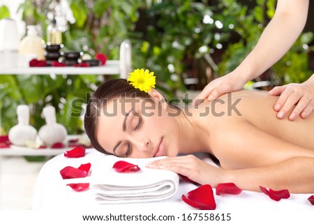 Spa girl. Beautiful young woman with flower in head lying on front while massage therapist massaging her back