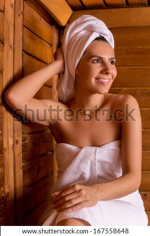 Beauty in sauna. Beautiful young woman wrapped in towel relaxing in sauna and smiling to you