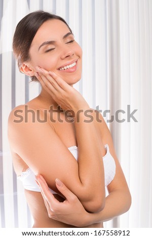 Sunbathing in solarium. Attractive young woman standing in tanning booth and touching face