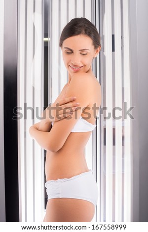 Beauty sunbathing. Side view of attractive young woman standing in tanning booth and keeping eyes closed