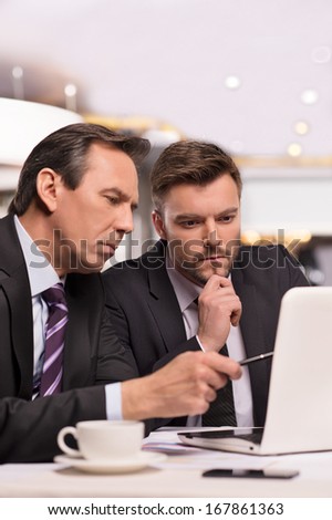 Discussing project. Two business people in formalwear discussing something while one of them pointing computer monitor