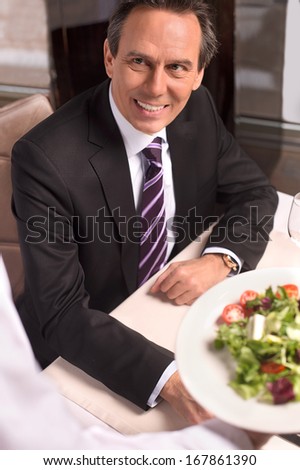 Man in restaurant. Top view of waiter holding a plate with salad while customer looking at him and smiling