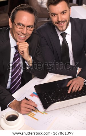Business people. Top view of two business people in formalwear smiling at camera while working on laptop