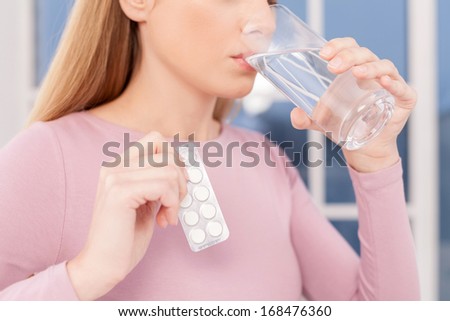 Taking pills. Cropped image of young woman taking pills and drinking water