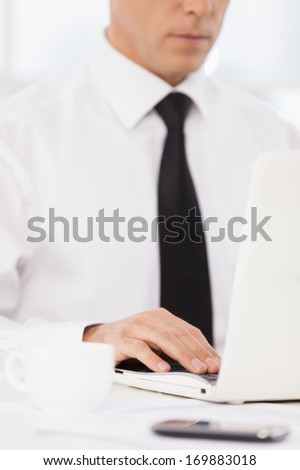 Businessman at work. Cropped image of confident mature man in shirt and tie using computer while sitting at his working place