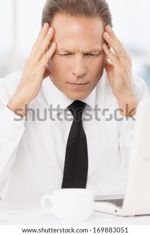 Tired of work. Depressed mature man in shirt and tie drinking holding head in hands while sitting at his working place