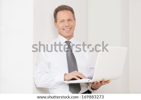 Businessman with laptop. Cheerful senior man in shirt and tie holding laptop and smiling at camera
