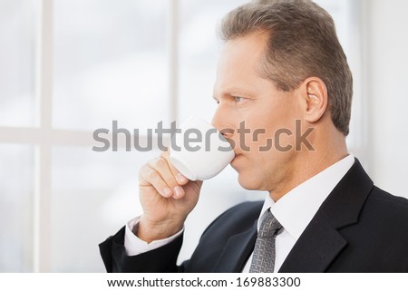 Break time. Side view of mature man in formalwear drinking coffee and looking through a window