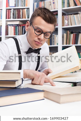 Preparation to the exam. Concentrated young nerd man in shirt and bow tie reading book and pointing it