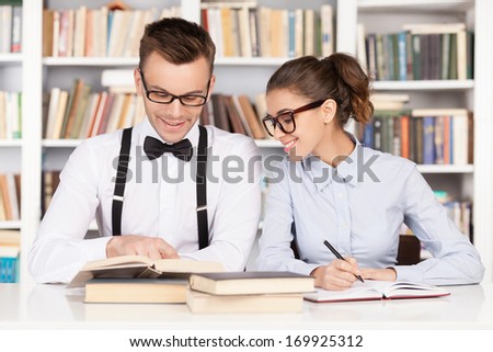 Studying together. Cheerful young nerd couple in glasses preparing to exams while sitting together at the library