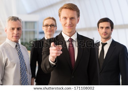 Will You Join Our Team? Confident Young Man In Formalwear Pointing You And Smiling While His Colleagues Standing Behind Him