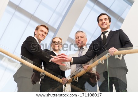 We are the best. Low angle view of four confident business people standing close to each other and holding hands together