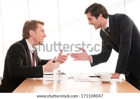 Business conflict. Two young men in formalwear arguing and gesturing while sitting at the table