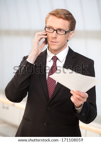 Businessman on the go. Confident senior man in formalwear talking on the mobile phone and holding the documents in his hand
