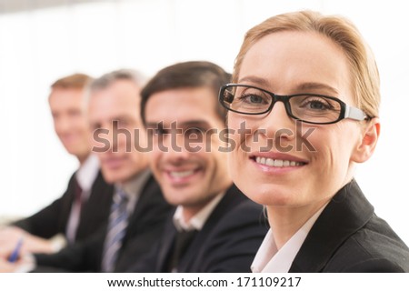 Only positive emotions. Four people in formalwear sitting together at the table and smiling at camera