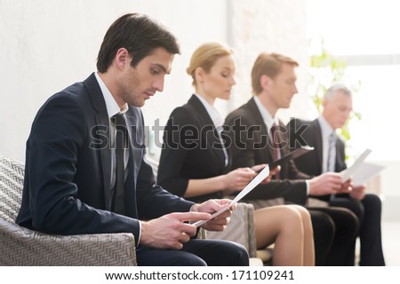 Job candidates. Four people in formalwear waiting in line while sitting at the chairs and holding papers in their hands