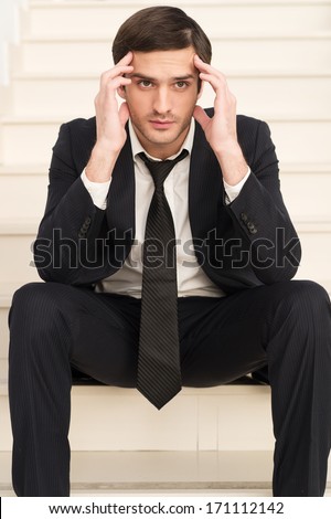 Depressed businessman. Depressed young man in formalwear holding head in hand and looking away while sitting on staircase