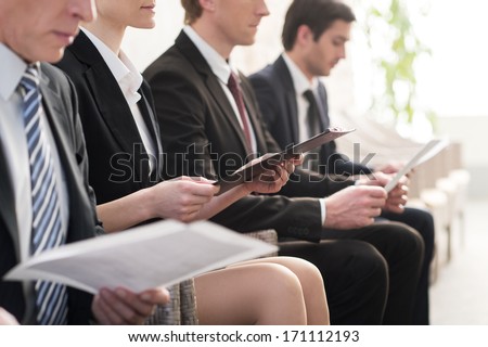 Waiting in line. Cropped image of people in formalwear waiting in line while sitting at the chairs and holding papers in their hands