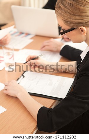 Woman at the business meeting. Top view of woman in formalwear writing something in her note pad while sitting at the business meeting