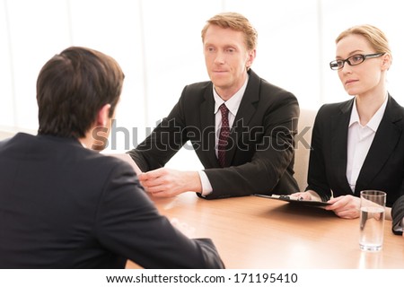 Job interview. Rear view of young man in formalwear sitting in front of two another business people