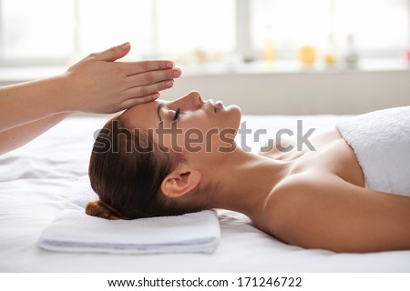 No stress. Beautiful young woman lying on back while massage therapist touching her forehead with hands