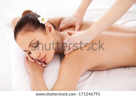 Massage for tired muscles. Top view of beautiful young woman lying on massage table and keeping eyes closed while massage therapist massaging her shoulders