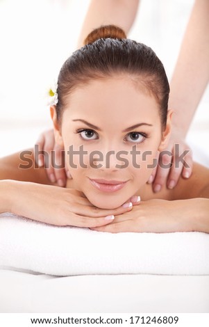 Day off at spa. Beautiful young woman lying on front and looking at camera while massage therapist massaging her shoulders
