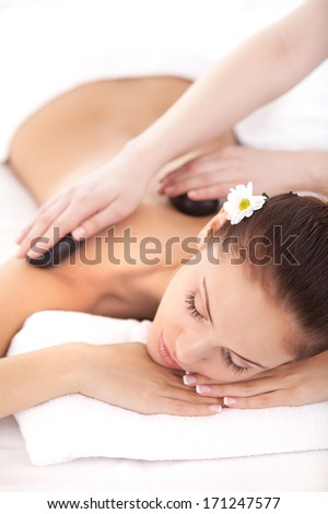 Hot stones for tired body. Top view of beautiful young woman lying on front while massage therapist massaging her back with spa stones