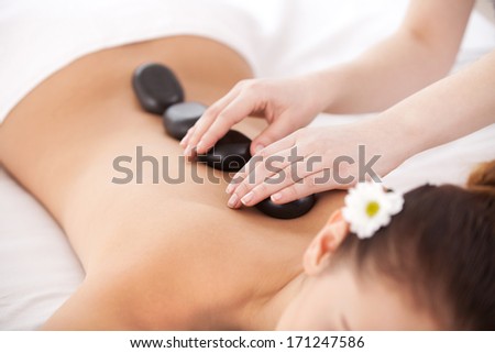 Beauty therapy. Top view of young woman lying on front while massage therapist massaging her back with spa stones