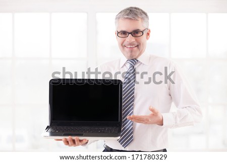 Your text here. Smiling senior man in shirt and tie holding laptop and pointing monitor
