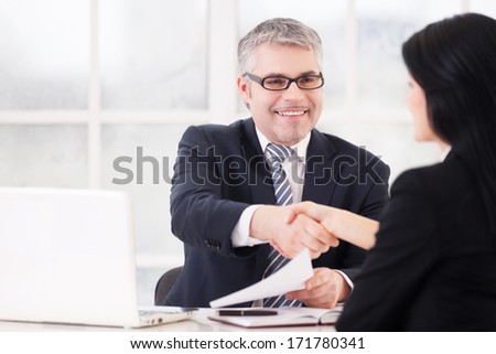 Great deal! Two business people handshaking and smiling while sitting face to face at the table