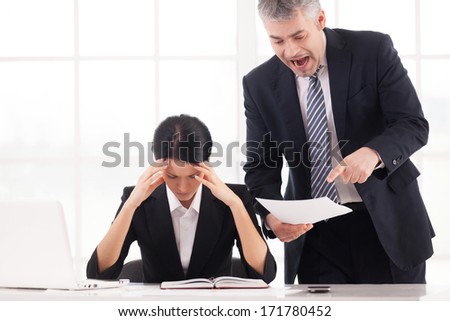 You are doing it all wrong! Furious mature businessman holding document and shouting while depressed woman sitting at the table and holding head in hands