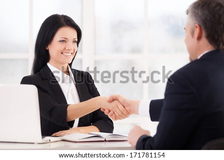Sealing a deal. Two cheerful business people handshaking and smiling while sitting face to face at the table