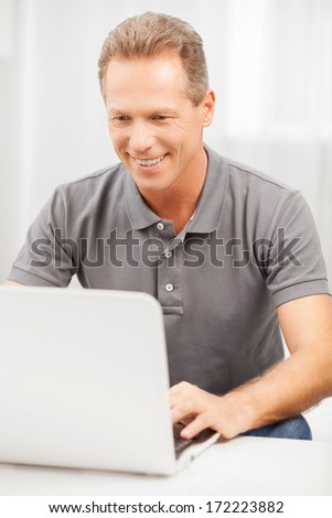 Man surfing web. Cheerful grey hair man in polo shirt using laptop and smiling