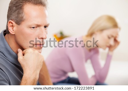 Depressed Couple. Side View Of Depressed Mature Man Holding Hand On Chin While Sad Woman Sitting On Background