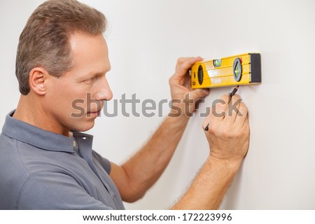 Taking wall measurements. Side view of confident mature man taking measurements of the wall