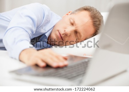 Overworked businessman sleeping. Senior man in formalwear holding hand on laptop keyboard while sleeping in bed
