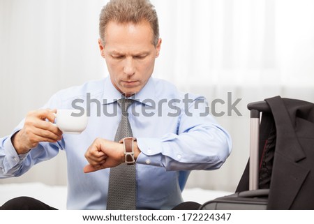 Executive in a hurry. Confident grey hair man in shirt checking the time while sitting on the bed