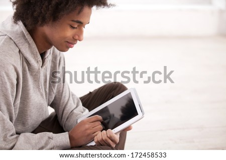 Teenager with digital tablet. Top view of African teenager working on digital tablet and while sitting on the floor
