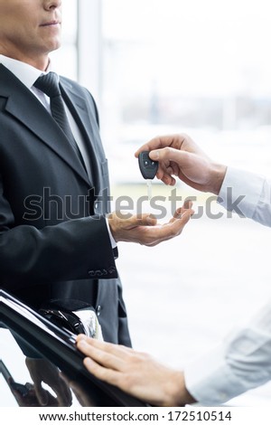 Giving a key to a new car owner. Cropped image of confident man in formalwear receiving a key from his new car