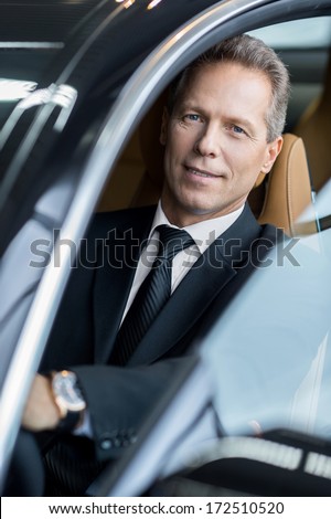 Business trip. Confident senior businessman sitting in car and smiling at camera