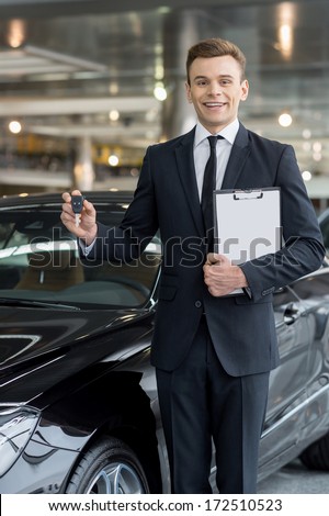 Good choice! Handsome young classic car salesman standing at the dealership and holding a key