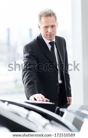 Making a right choice. Confident grey hair man in formalwear examining car at the dealership